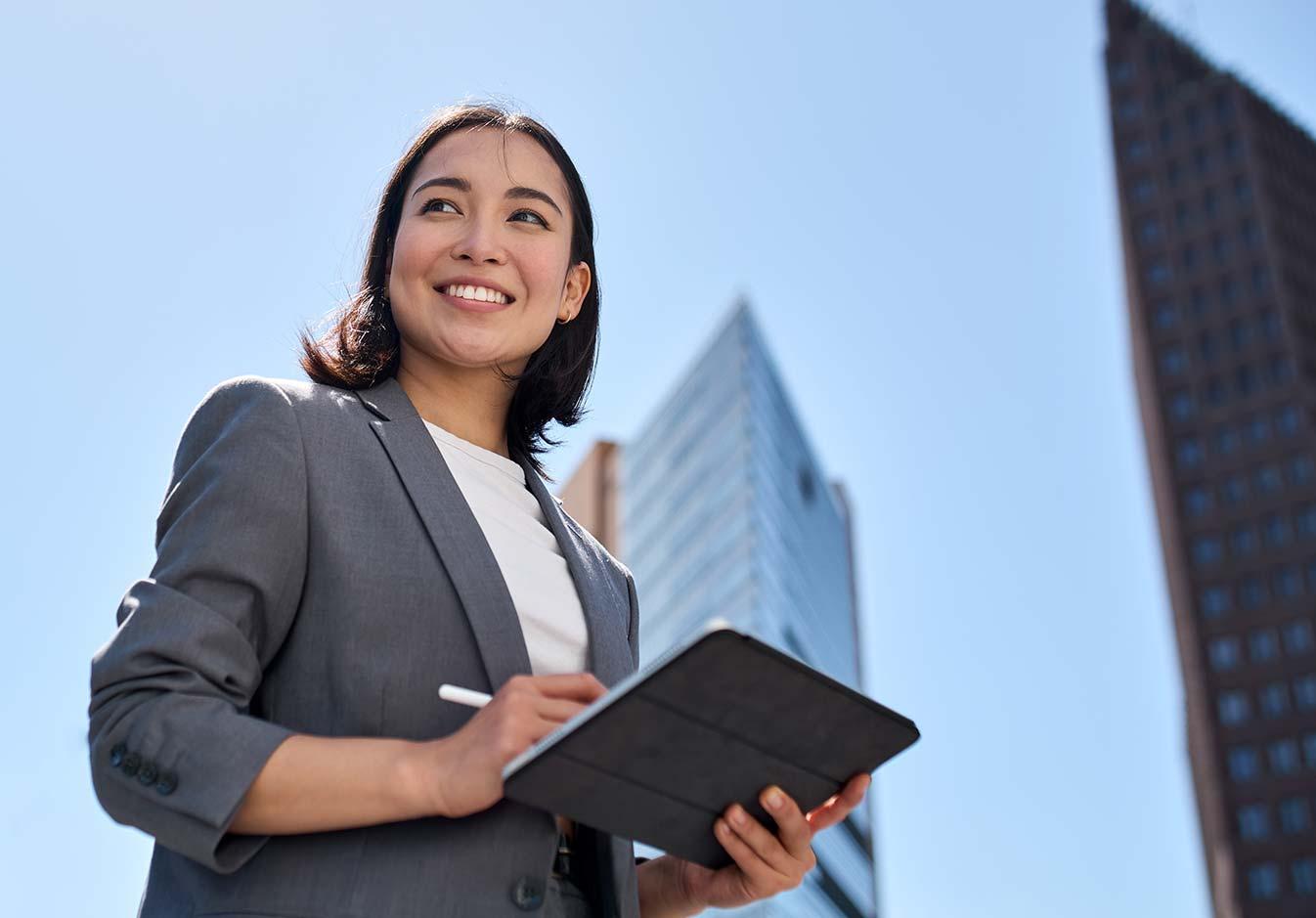 Confident young professional holding a tablet outdoors with skyscrapers in the background