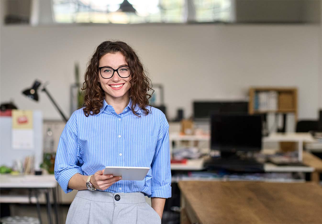 Smiling woman with glasses holding a tablet in a modern office