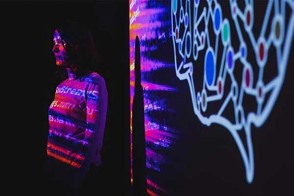 Person illuminated by colorful digital projections beside an abstract brain graphic.