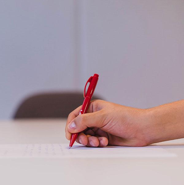 Hand writing on a document with a red pen.
