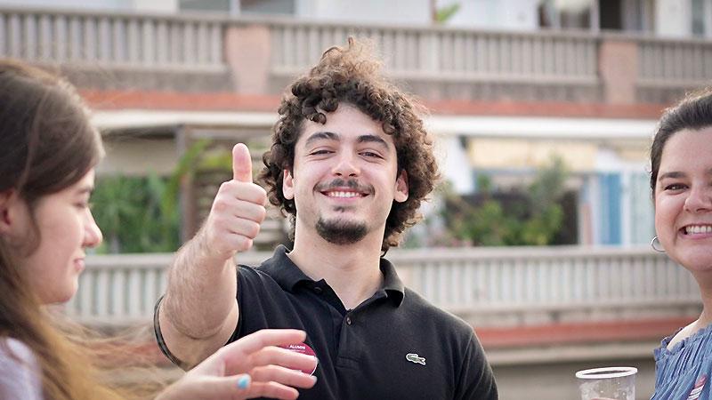 Student smiling and giving a thumbs-up gesture during an outdoor social event.